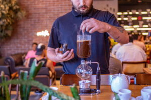Un barista utiliza una cafetera de sifón en una cafetería moderna. Minijob en Alemania: límite de ingresos, salario, horas y sectores explicados para quienes buscan oportunidades laborales.