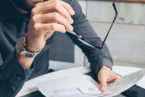 Un hombre con traje sostiene sus gafas en la mano izquierda y revisa documentos. La Riester-Pensión en Alemania cambia desde 2027: conoce sus ventajas, limitaciones y lo que deben saber los trabajadores.
