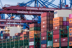 Puerto de Hamburgo: contenedores marítimos apilados y grúas en la terminal Burchardkai. Trabajo en Alemania: el mercado laboral mejora y crecen las oportunidades en tecnología, TI, hotelería, logística, salud e industria.