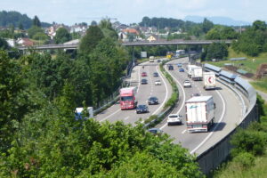 Autopista sinuosa en un paisaje verde, con tráfico denso y fluido y diversos camiones. Alemania busca hasta 120.000 camioneros por jubilaciones. Las empresas aumentan sueldos y ofrecen turnos familiares para atraer choferes del exterior.